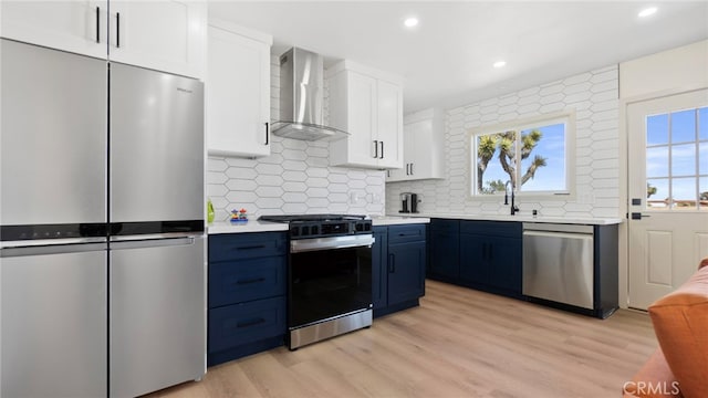 kitchen featuring light wood finished floors, light countertops, blue cabinets, appliances with stainless steel finishes, and wall chimney exhaust hood