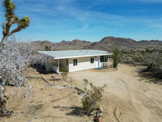 rear view of house featuring a mountain view, driveway, and stucco siding