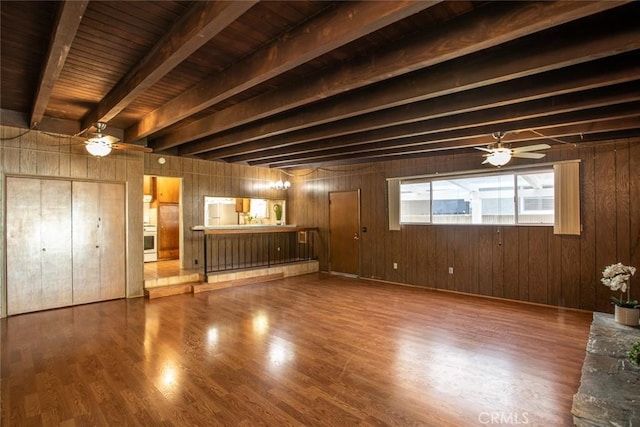 unfurnished living room featuring beam ceiling, wood walls, wood finished floors, and a ceiling fan