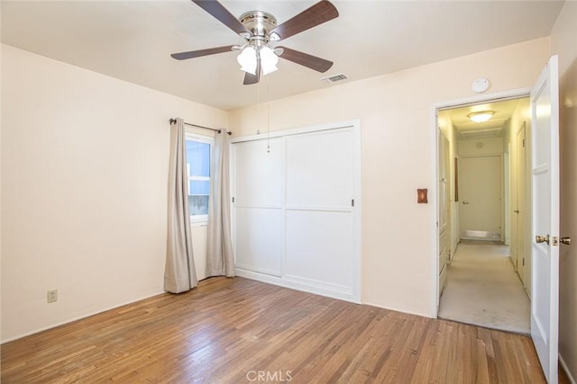 unfurnished bedroom featuring a closet, visible vents, ceiling fan, and light wood-style flooring