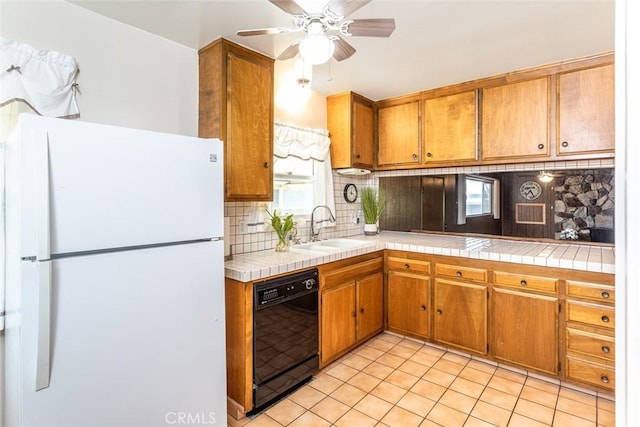 kitchen featuring a sink, decorative backsplash, tile counters, freestanding refrigerator, and dishwasher