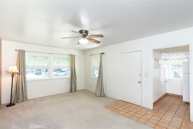 unfurnished room with light carpet, light tile patterned floors, and a ceiling fan