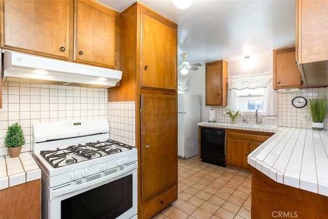 kitchen featuring under cabinet range hood, white appliances, a sink, tile counters, and brown cabinets