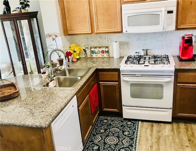 kitchen featuring a peninsula, white appliances, wood finished floors, a sink, and backsplash