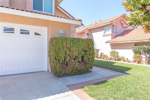 property entrance featuring a garage, a tile roof, a yard, and stucco siding