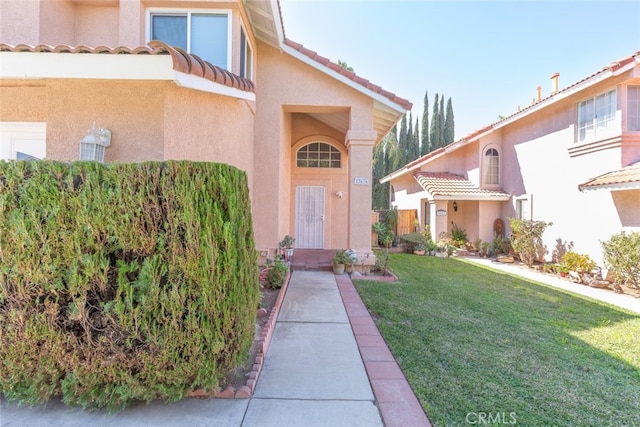 view of exterior entry featuring a tiled roof, a lawn, and stucco siding