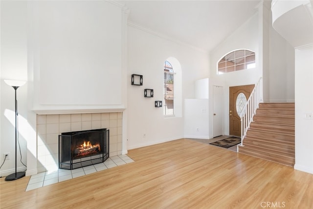 foyer entrance featuring baseboards, a tile fireplace, stairway, wood finished floors, and high vaulted ceiling