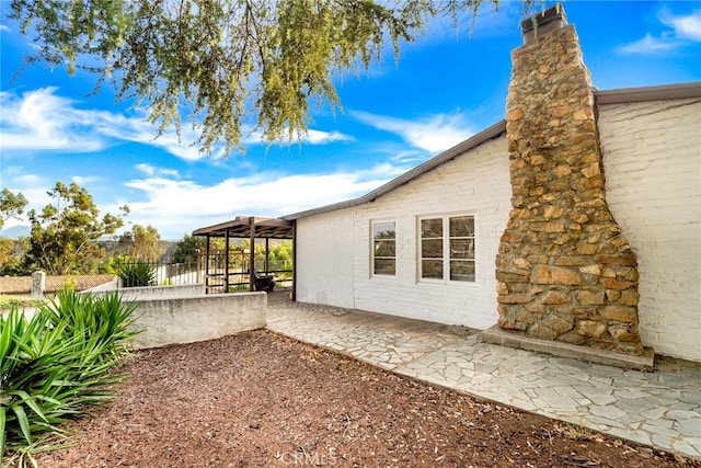 view of home's exterior with a patio area, a chimney, fence, and a gazebo