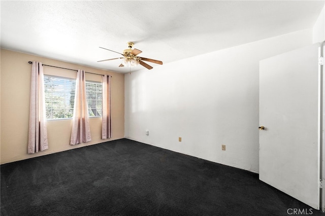 spare room featuring a ceiling fan and dark carpet