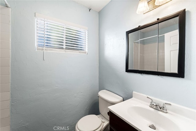 bathroom featuring a textured wall, walk in shower, vanity, and toilet