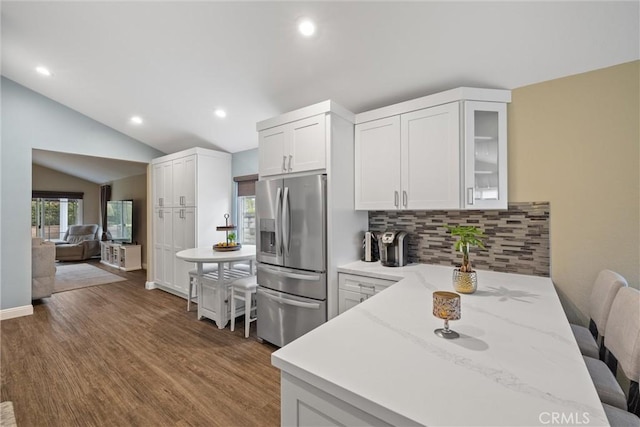 kitchen with tasteful backsplash, lofted ceiling, wood finished floors, light stone countertops, and stainless steel refrigerator with ice dispenser