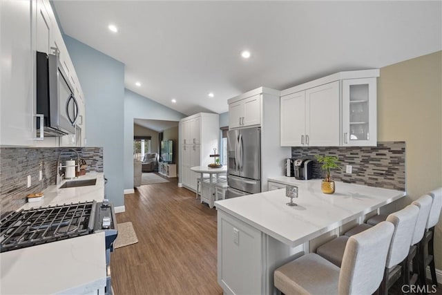 kitchen featuring wood finished floors, a peninsula, vaulted ceiling, stainless steel appliances, and a sink