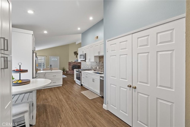 kitchen featuring white cabinets, vaulted ceiling, appliances with stainless steel finishes, decorative backsplash, and dark wood-style floors