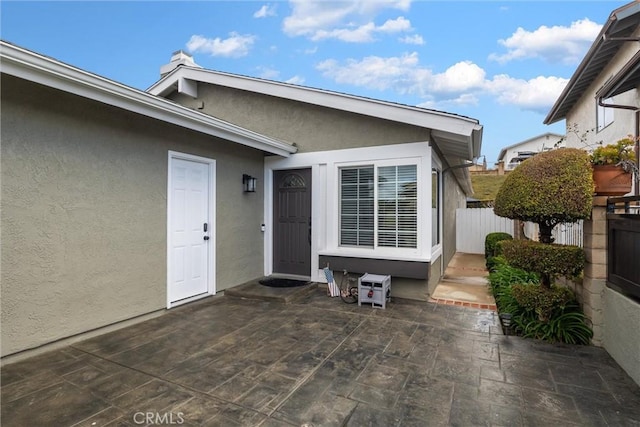 property entrance with a patio area, fence, and stucco siding