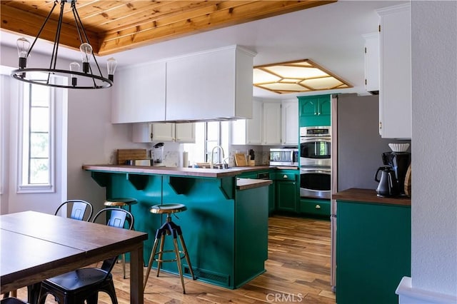 1075 Rivera Dr, Wrightwood, CA 92397 - kitchen featuring a breakfast bar area, wood finished floors, wood ceiling, appliances with stainless steel finishes, and green cabinetry