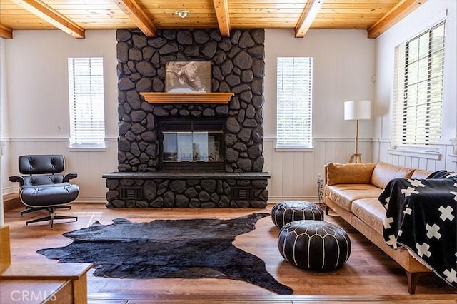 living room with wood ceiling, wood finished floors, a stone fireplace, and wainscoting