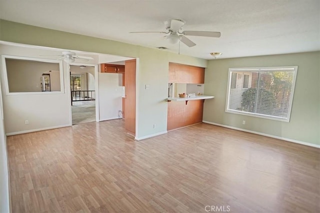 unfurnished living room with light wood finished floors, baseboards, and a ceiling fan