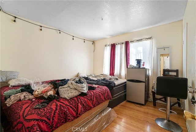 bedroom featuring light wood-style floors and freestanding refrigerator