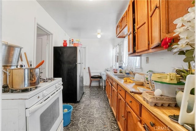 kitchen with brown cabinets, light countertops, freestanding refrigerator, a sink, and white range with gas stovetop