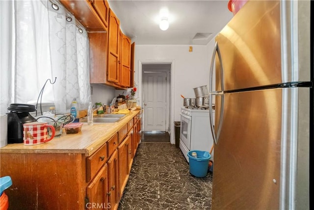 kitchen with brown cabinets, white gas range, light countertops, freestanding refrigerator, and a sink