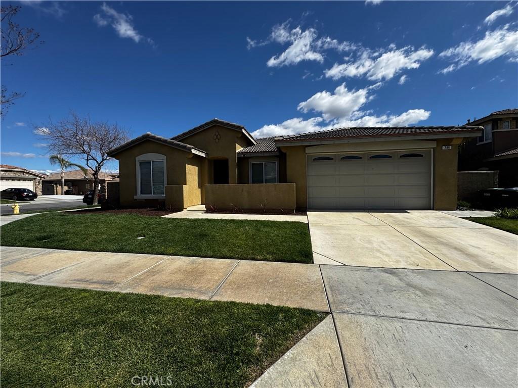 view of front of house featuring an attached garage, driveway, a tiled roof, stucco siding, and a front lawn