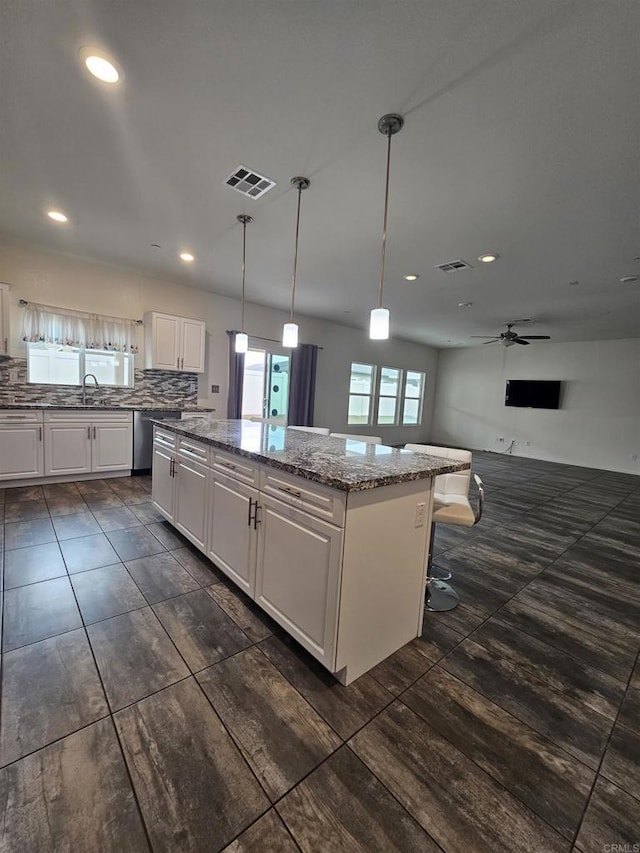 kitchen featuring visible vents, a kitchen island, light stone counters, white cabinetry, and a sink