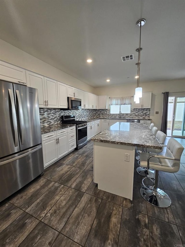 kitchen featuring a kitchen bar, visible vents, backsplash, white cabinetry, and stainless steel appliances