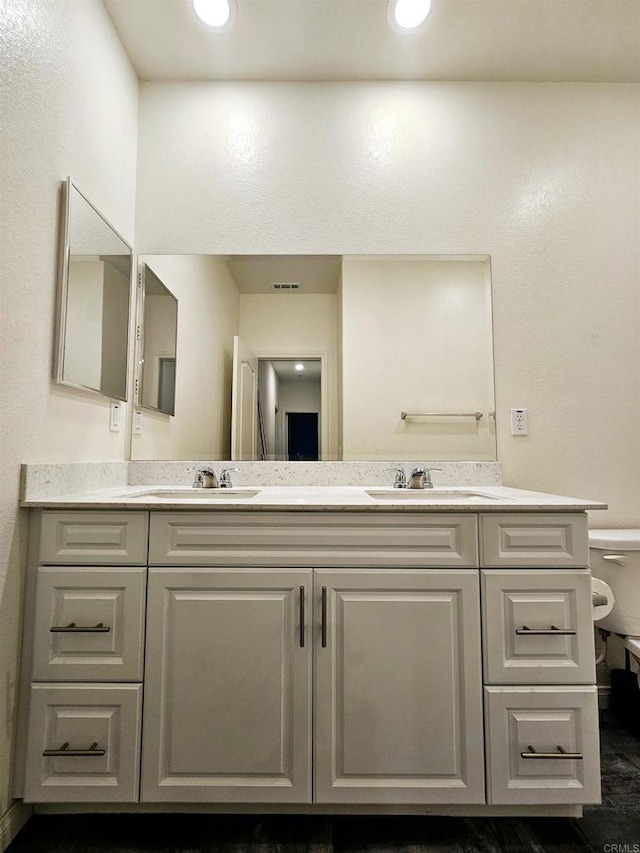 bathroom with a sink, toilet, and double vanity