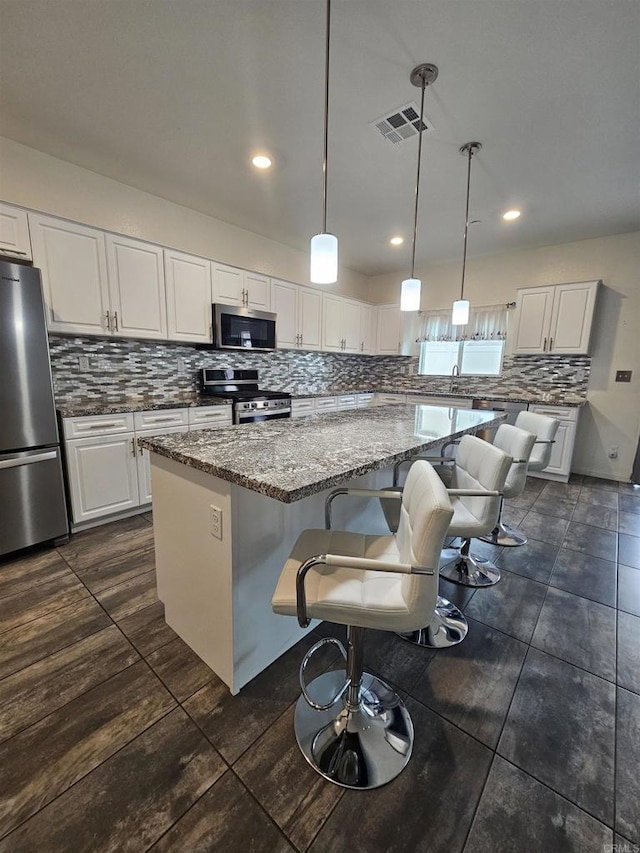 kitchen with a kitchen island, backsplash, visible vents, appliances with stainless steel finishes, and white cabinetry