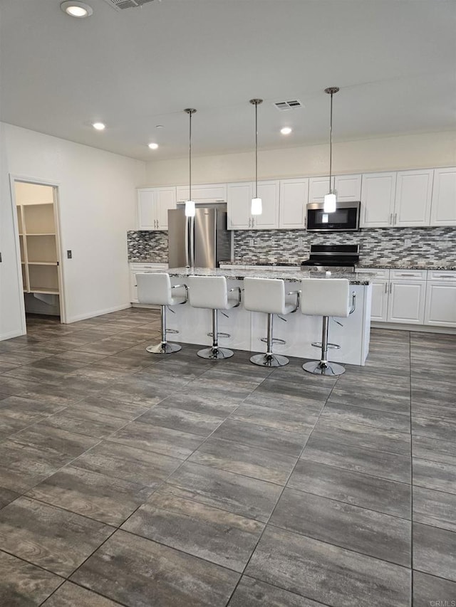 kitchen with backsplash, white cabinetry, appliances with stainless steel finishes, and a kitchen bar