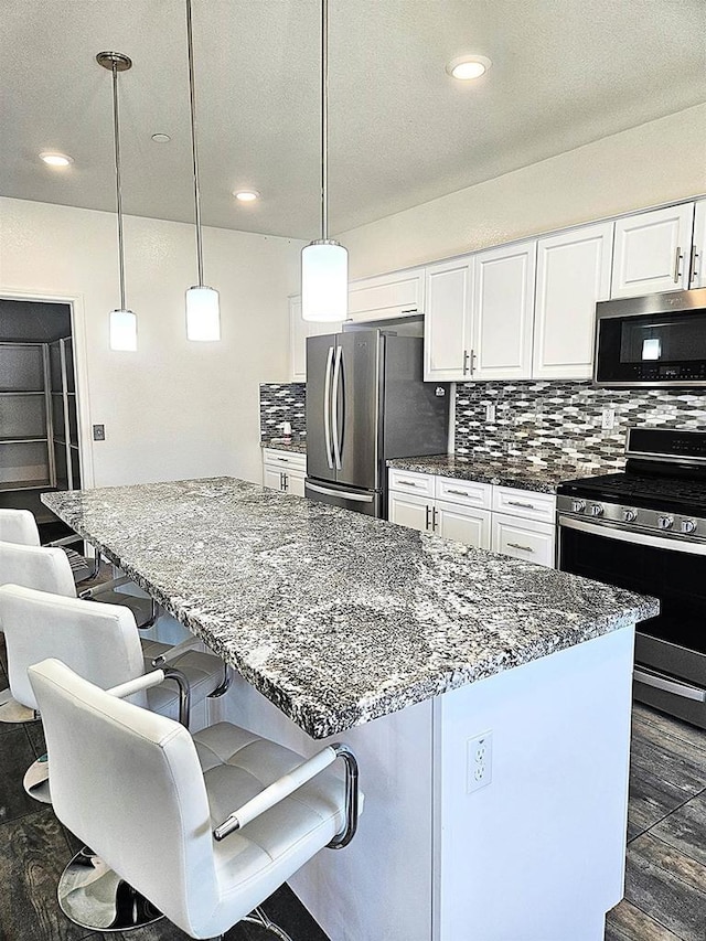 kitchen with white cabinetry, dark stone countertops, tasteful backsplash, and stainless steel appliances