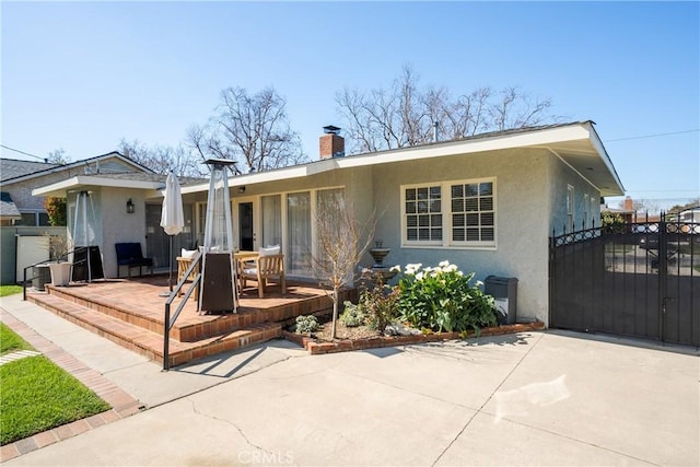 back of house featuring a gate, fence, a chimney, stucco siding, and a patio area