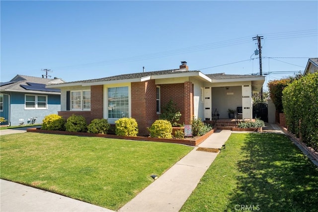 single story home featuring brick siding, a chimney, and a front yard