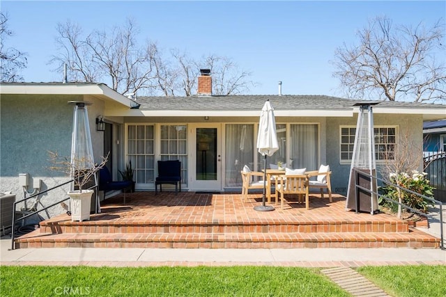 back of property featuring stucco siding, roof with shingles, a chimney, and a patio area