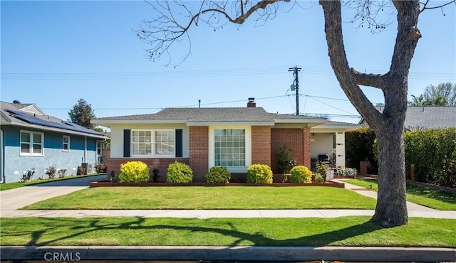 view of front of home featuring brick siding, driveway, a chimney, and a front lawn