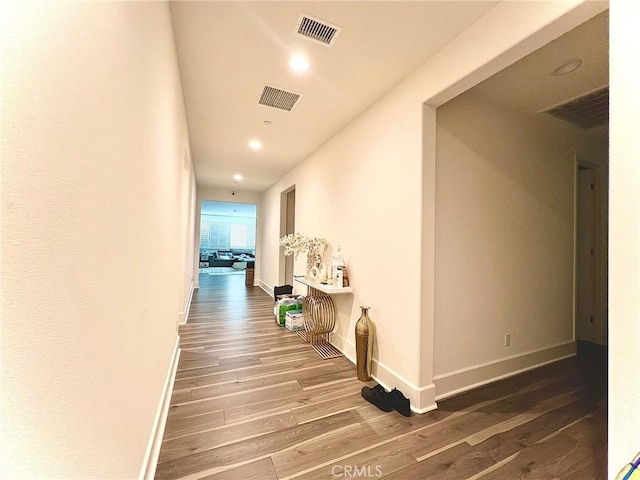 hall featuring wood finished floors, visible vents, and baseboards