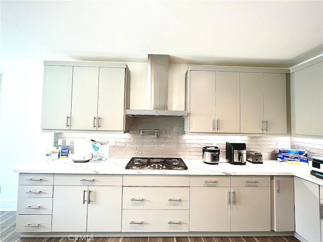 kitchen featuring gray cabinetry, wall chimney exhaust hood, backsplash, and stainless steel gas stovetop