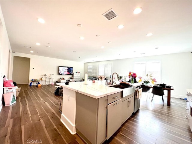 kitchen featuring visible vents, dark wood finished floors, a sink, a kitchen island with sink, and stainless steel dishwasher