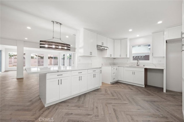 kitchen with under cabinet range hood, white cabinets, a sink, and recessed lighting