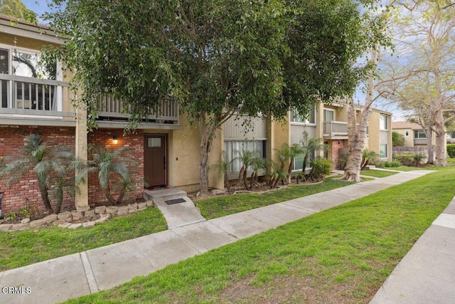 view of property featuring stucco siding, a front yard, and brick siding