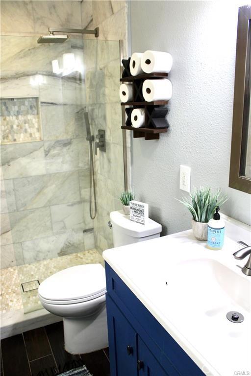 bathroom featuring toilet, a textured wall, a tile shower, and vanity