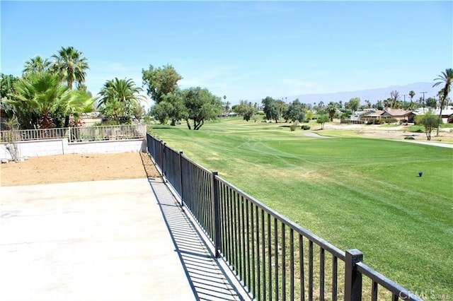 view of community with a mountain view, view of golf course, fence, and a lawn