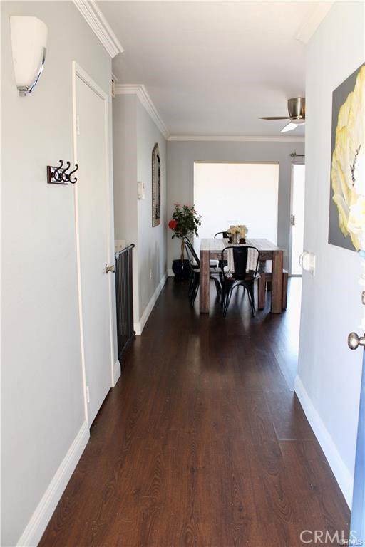 corridor with dark wood-style floors, ornamental molding, and baseboards