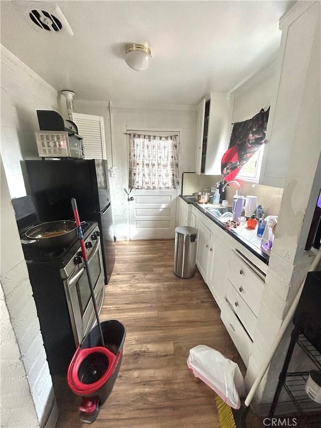 kitchen featuring white cabinets, wood finished floors, crown molding, stainless steel range with electric stovetop, and a sink