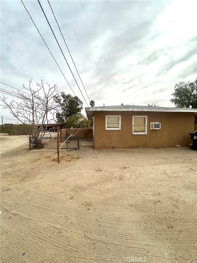 view of side of property with a wall mounted AC, fence, and stucco siding