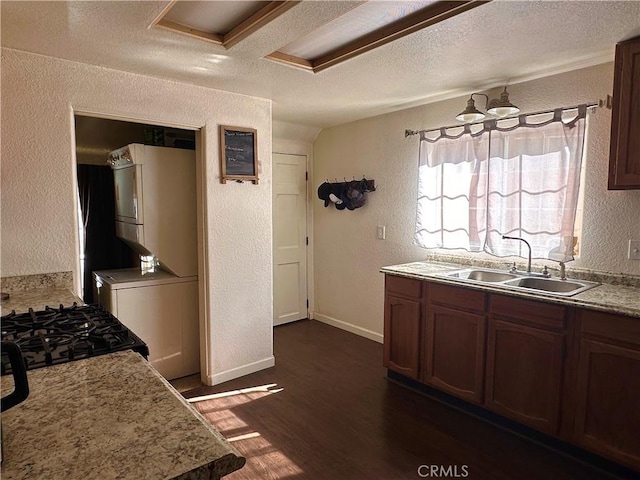 kitchen featuring stacked washer / dryer, a textured ceiling, a sink, and a textured wall