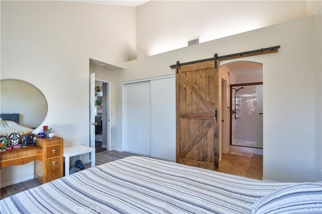 bedroom featuring visible vents, a barn door, arched walkways, a high ceiling, and a closet