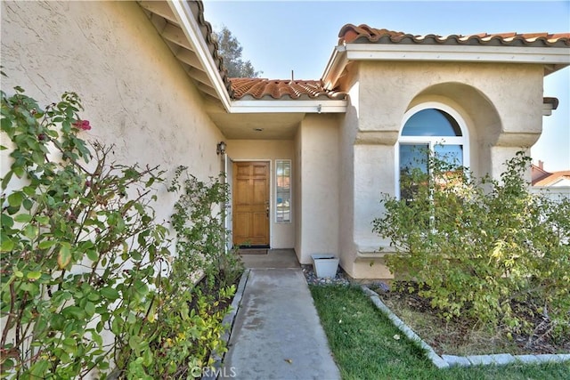 view of exterior entry with stucco siding and a tiled roof