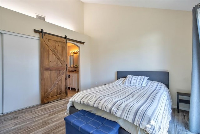 bedroom featuring a barn door, arched walkways, visible vents, and wood finished floors