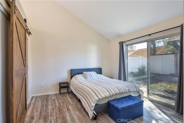 bedroom featuring wood finished floors, a barn door, baseboards, access to exterior, and vaulted ceiling